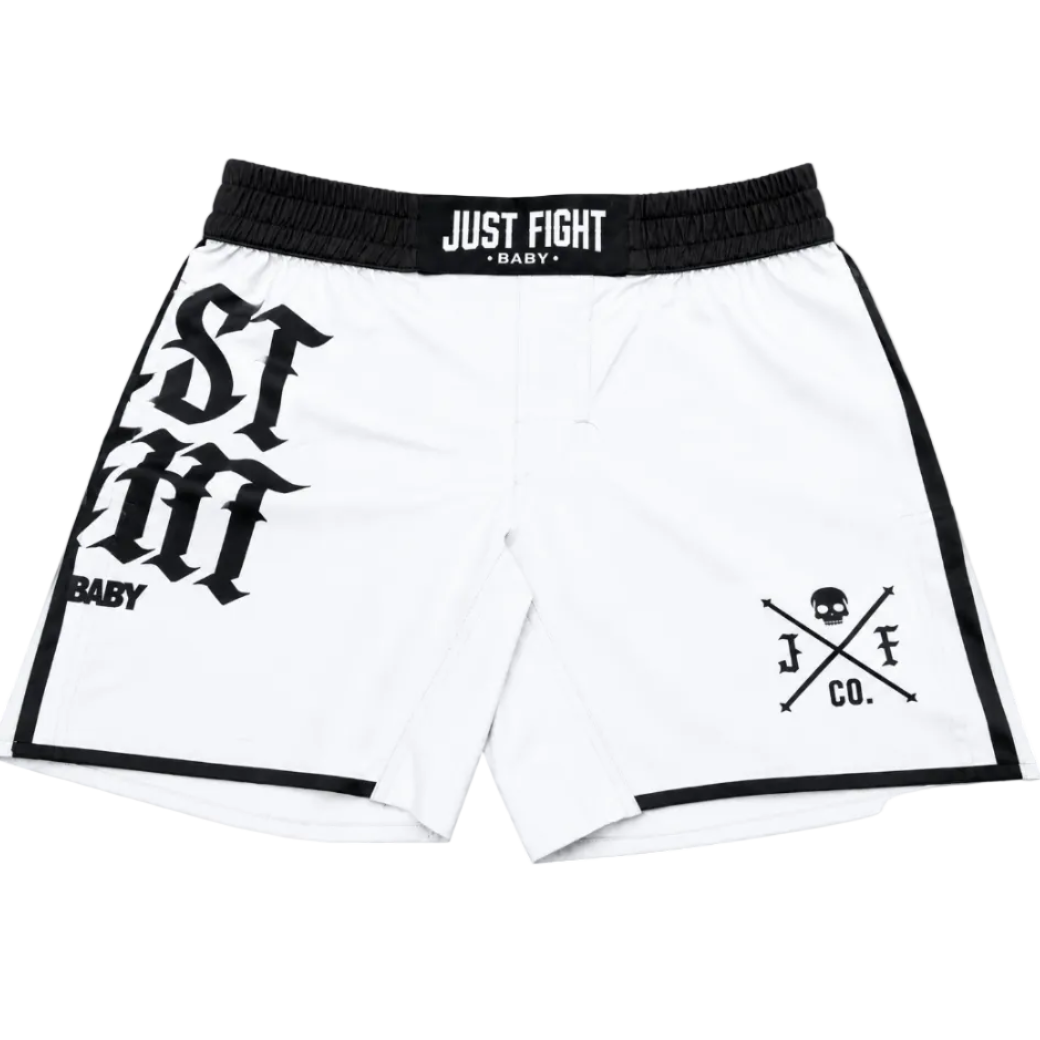 White athletic shorts with a black elastic waistband featuring the text 'JUST FIGHT BABY'. The left leg features a large black gothic font graphic, and the right leg has a black logo with a skull and crossed elements reading 'J.